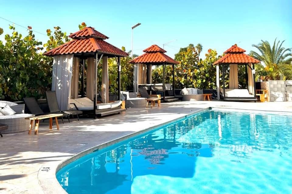 Resort pool area with covered cabanas with red-tile roofs and palm tree landscaping