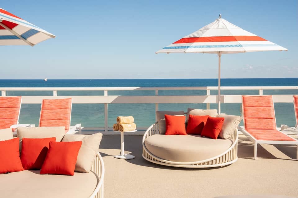 Beachfront deck with modern lounge seating, umbrellas, and ocean horizon view