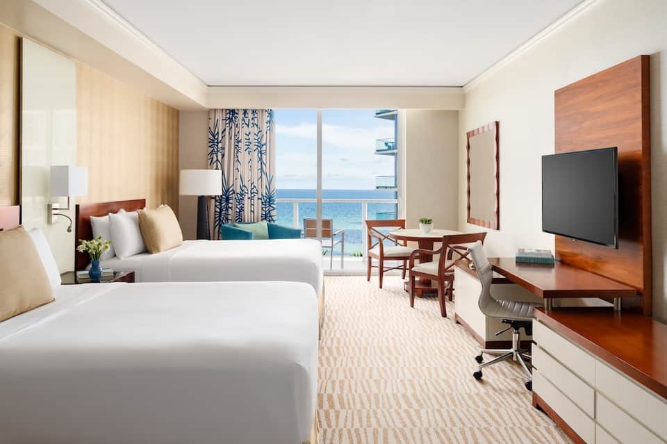 Hotel room with two queen beds, ocean view balcony, and modern furnishings