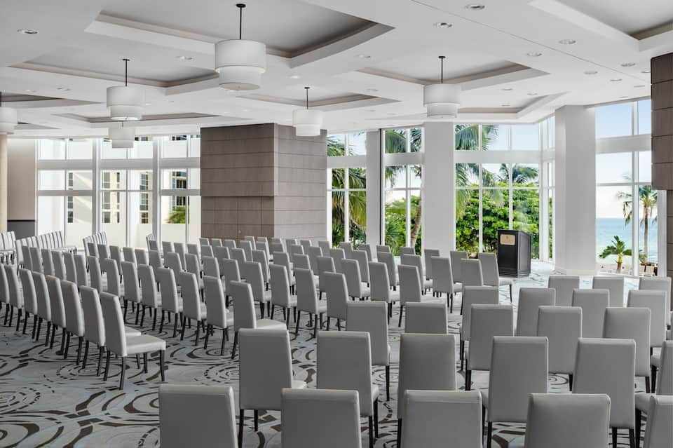 Beachfront conference space with rows of white chairs and ocean view through large windows