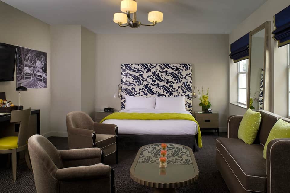 Contemporary hotel room with patterned headboard, lime green accent blanket, brown armchairs, and modern fixtures
