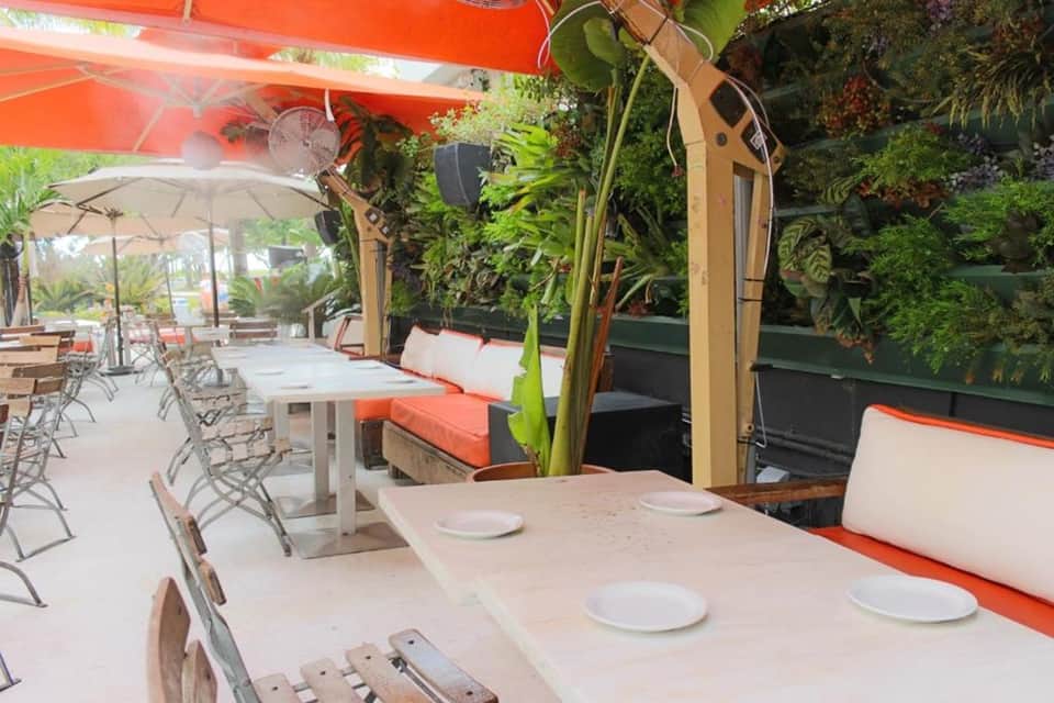 Outdoor dining area with white tables, orange umbrellas, and green living walls