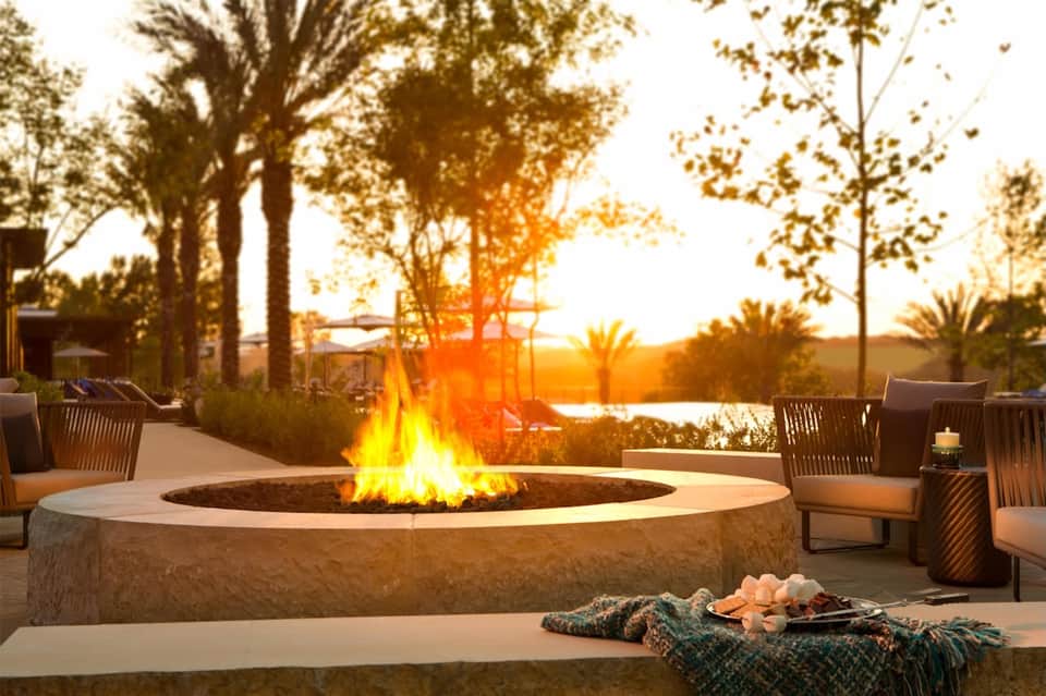 Waterfront firepit gathering area at dusk with lounge chairs, palm trees, and water views