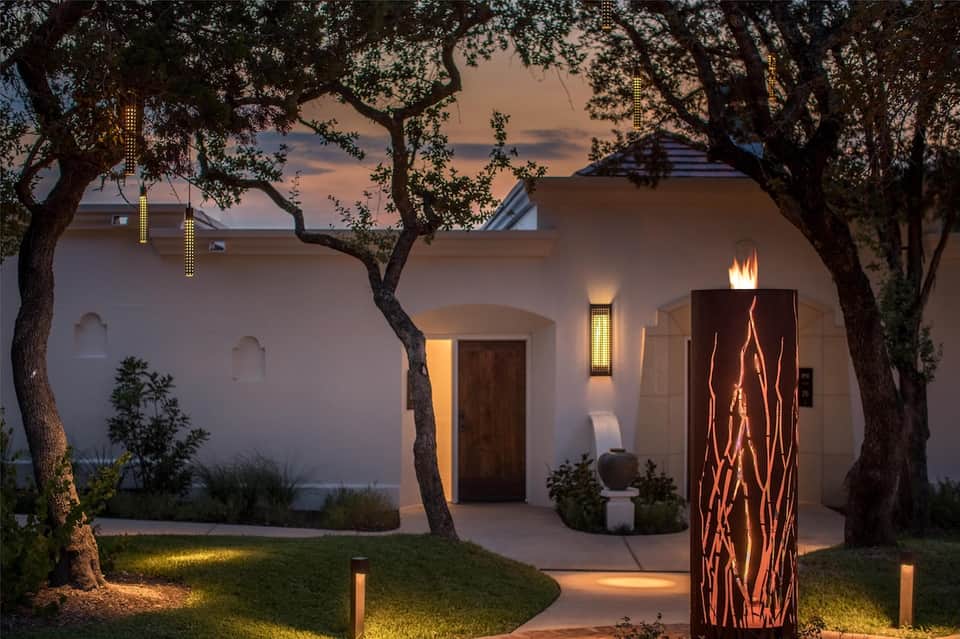 Modern home exterior at twilight with mature oak trees, uplighting, and illuminated architectural features
