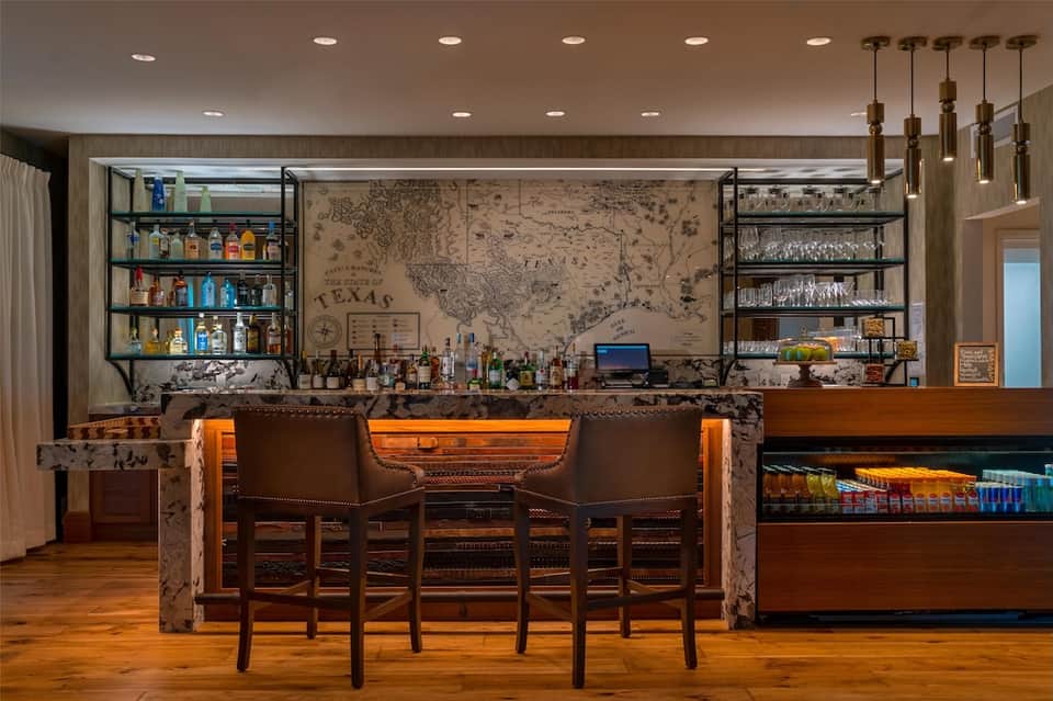 Sophisticated bar with leather upholstered seating, Texas map wall art, glass shelving, and brass fixtures