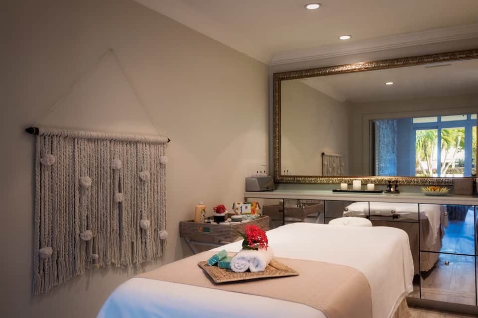 Spa treatment room with two massage tables, framed mirror, and macramé wall hanging