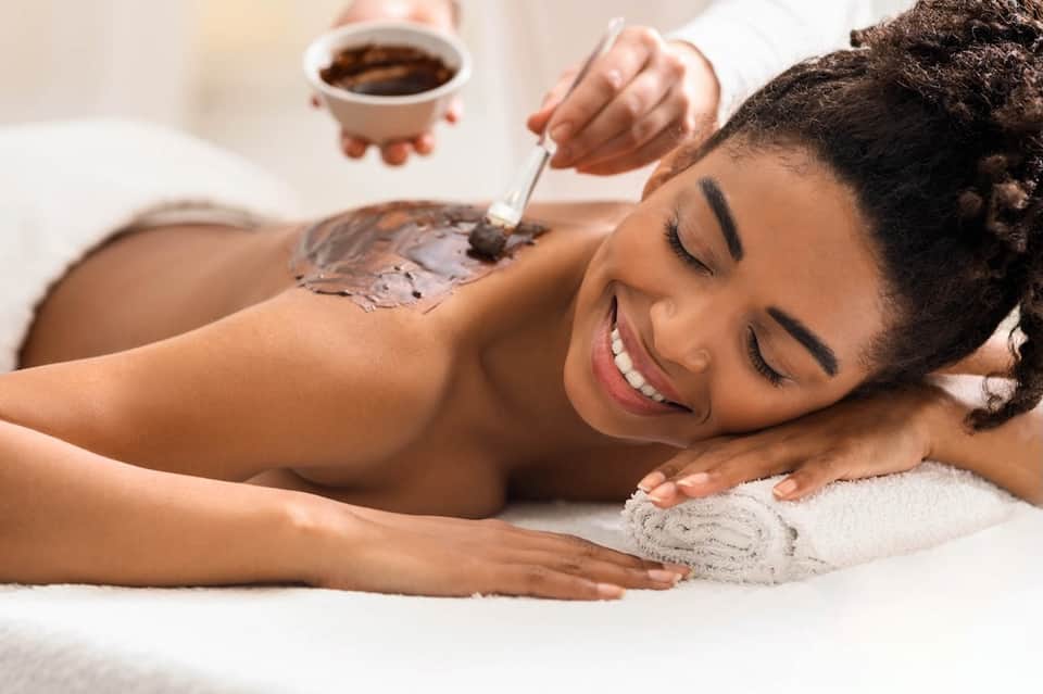 Spa treatment showing chocolate body mask application on relaxed guest with coffee nearby