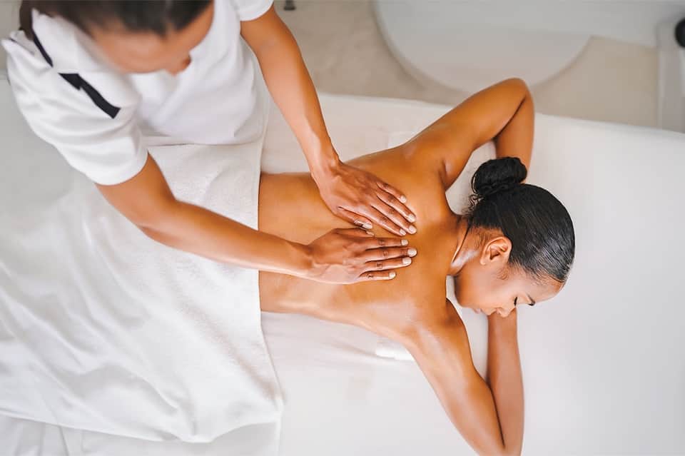 Spa therapist providing back massage to guest in white towel on massage table