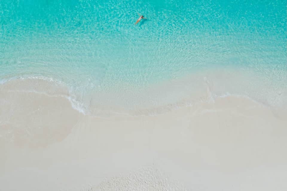 Aerial view of pristine turquoise ocean water with swimmer and white sandy beach