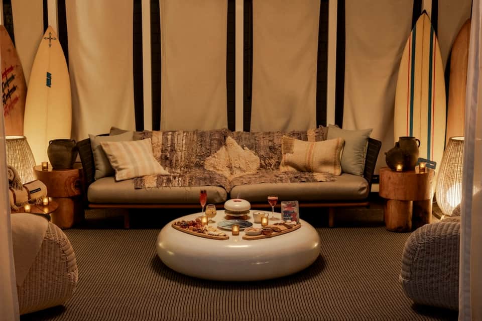 Lounge area with coastal decor, surfboards, leather sofa, and round white ottoman with snacks