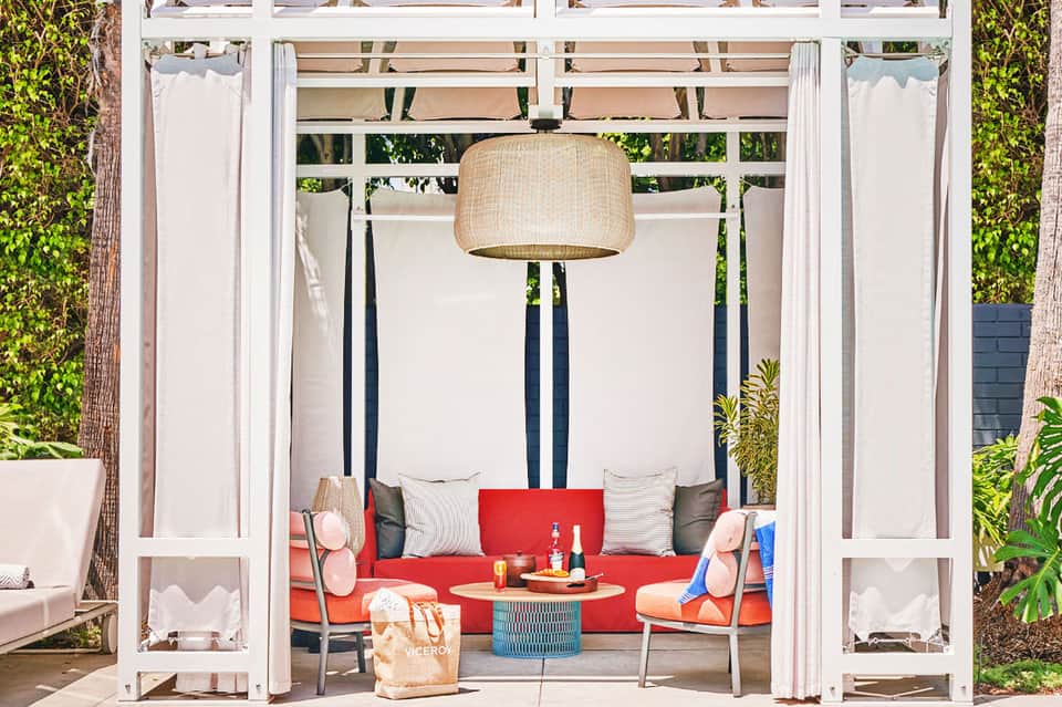 Modern cabana with red cushioned seating, white drapes, and pendant lighting