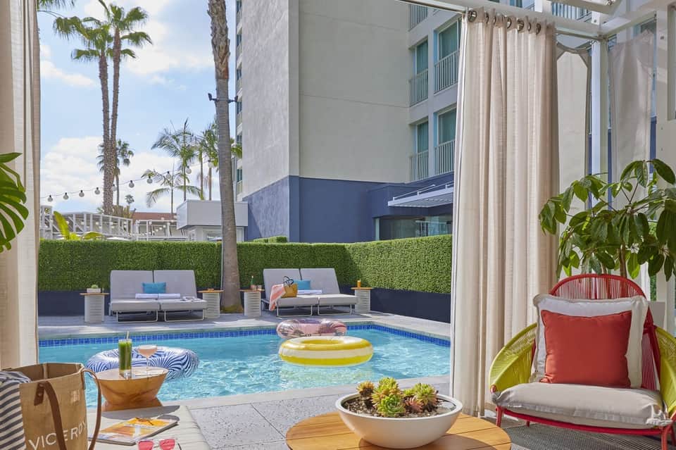 Modern resort pool area with yellow inflatable toy, lounge seating, palm trees, and high-rise buildings