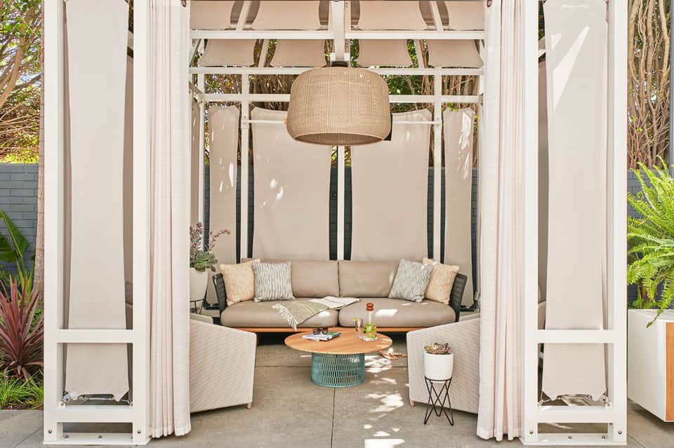 Luxury outdoor cabana with curved seating, hanging woven lamp, side tables, and semi-enclosed design