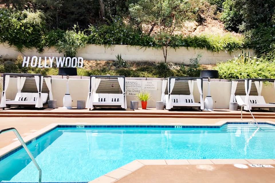 Resort pool with white cabanas and Hollywood sign visible on hillside behind property