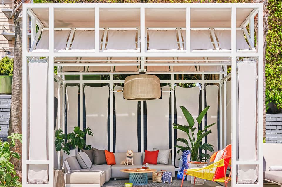 Modern outdoor lounge with white pergola, gray seating, plants, and decorative elements