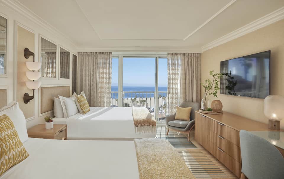 Luxurious oceanview hotel room with two queen beds, balcony, beige decor, and panoramic sea views