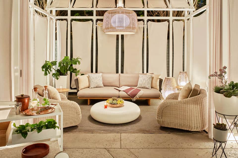 Covered outdoor lounge with wicker furniture, beige sofa, round coffee table, and hanging pendant lamp