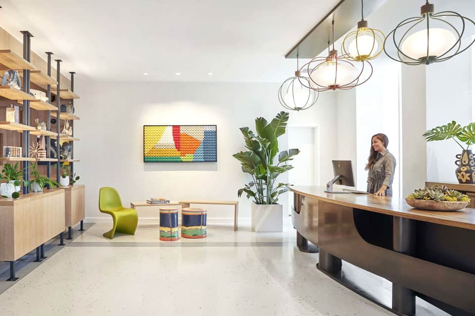 Hotel lobby reception desk with modern design, plants, pendant lights, and check-in counter