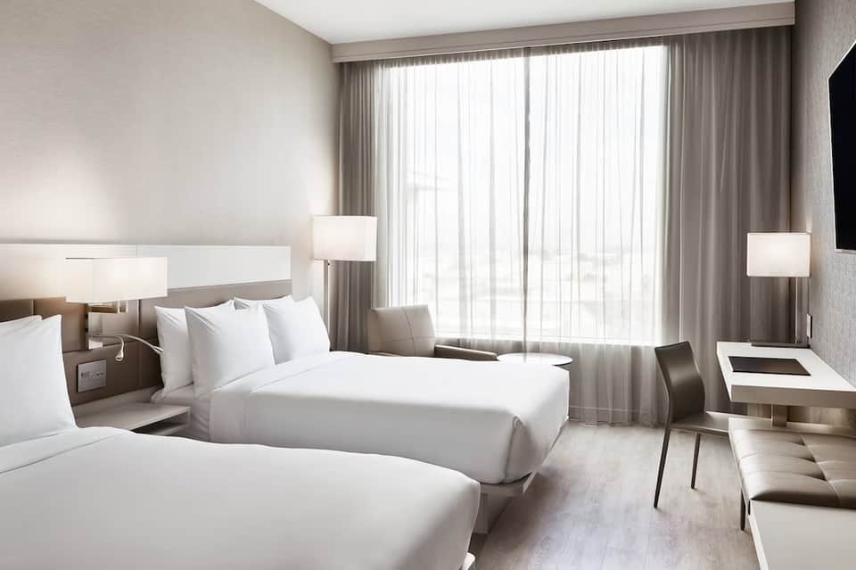 Hotel bedroom with two queen beds, floor-to-ceiling curtains, modern lighting, and contemporary furnishings