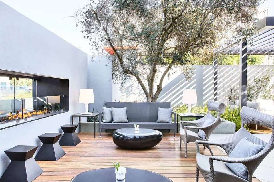 Modern outdoor patio with fireplace, gray lounge seating, fire pits, wooden deck, and slatted privacy screens
