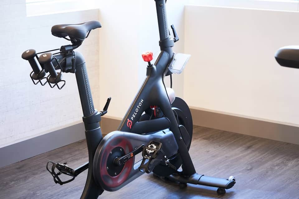 Peloton stationary exercise bike with red accents in bright, minimalist fitness studio space