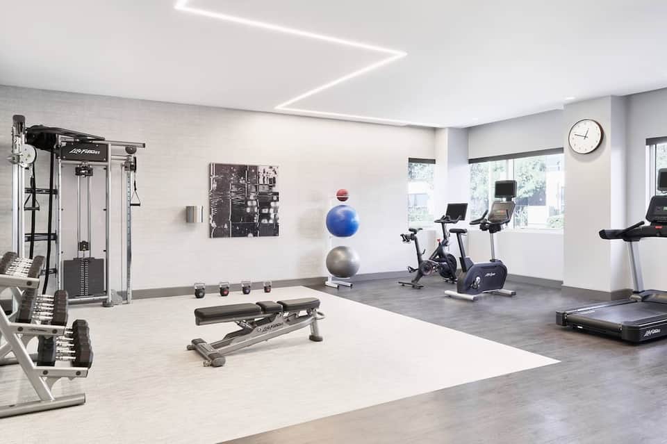Modern fitness center with white brick walls, exercise equipment, bikes, and large windows with natural lighting.