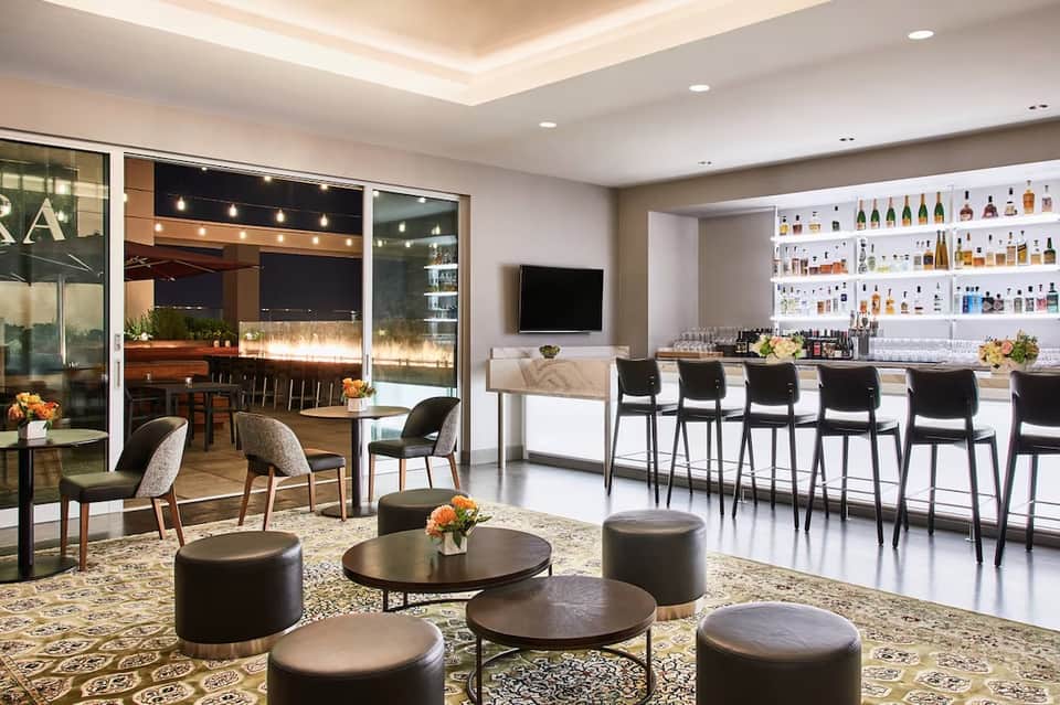 Upscale hotel bar lounge with full liquor shelves, seating area, outdoor terrace view, contemporary design aesthetic