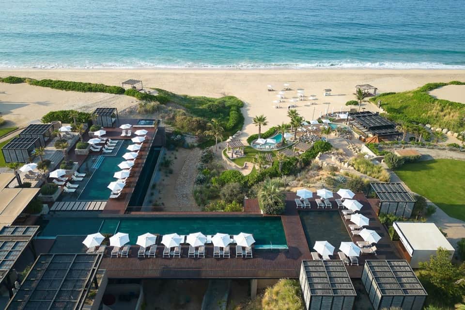 Aerial view of beachfront resort with multiple pools and white umbrellas overlooking ocean