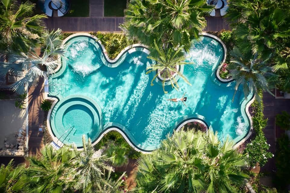 Overhead view of shaped resort pool surrounded by palm trees and tropical landscape