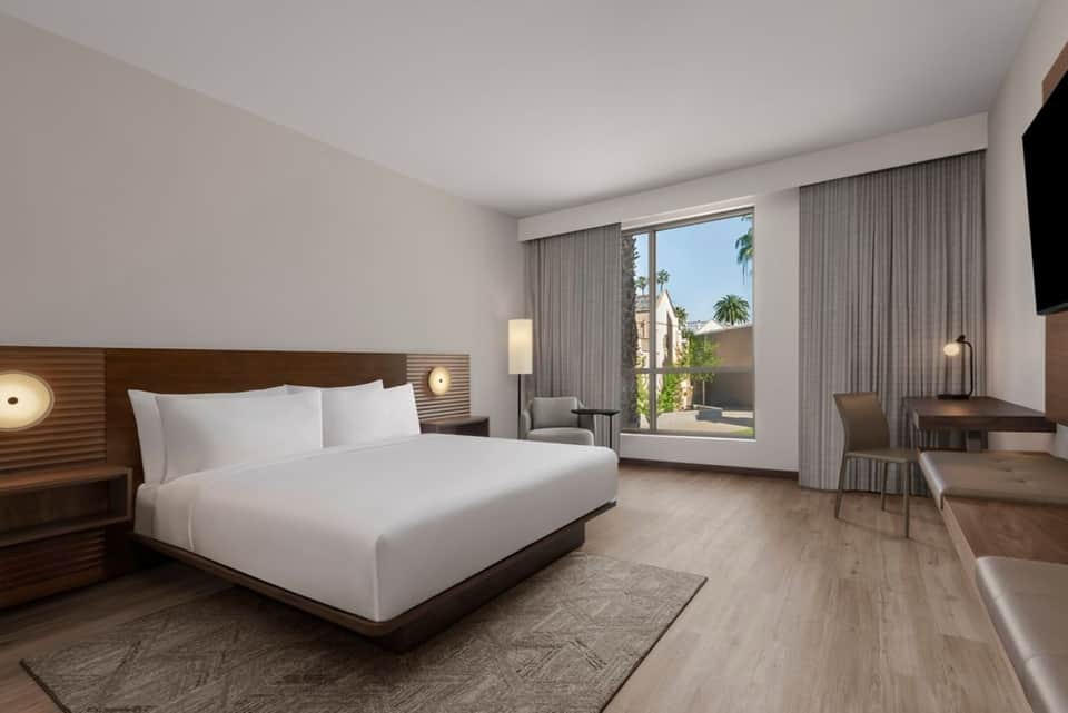 Modern hotel bedroom with king bed, balcony, contemporary furnishings, and warm lighting