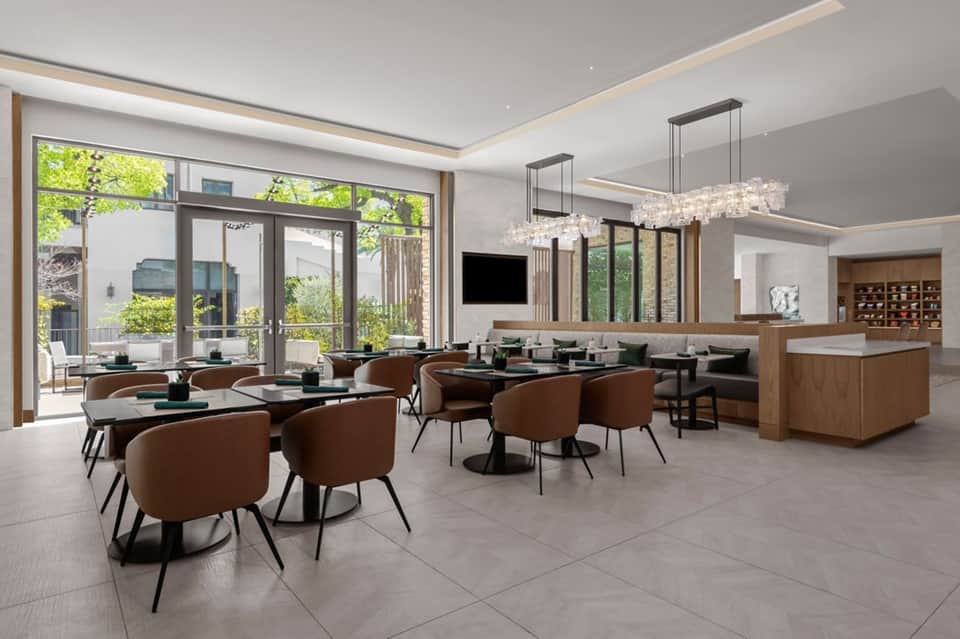 Contemporary hotel lobby with dining area, earth-tone seating, crystal chandeliers, and large windows