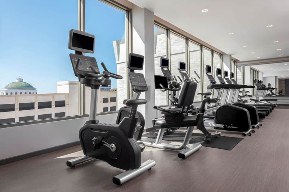 Modern fitness center with exercise bikes and equipment facing floor-to-ceiling windows and city skyline view