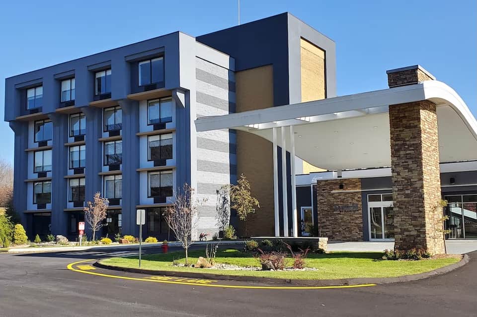 Modern hotel exterior featuring blue facade, white entrance canopy, brick chimney, and curved driveway