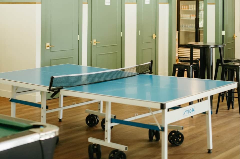 Recreation room with blue ping-pong table, green panel walls, wooden flooring, and seating areas