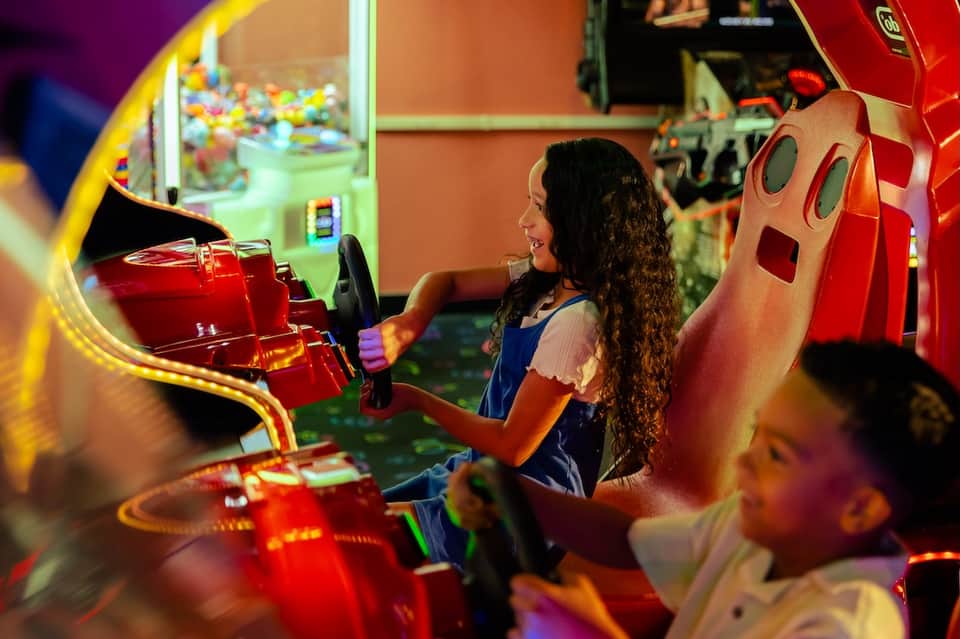 Child playing racing arcade game in colorful lit game room with neon signs and entertainment machines