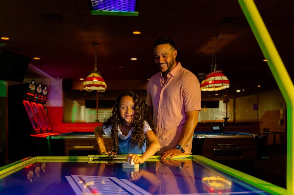 Father and daughter playing air hockey in colorful arcade game room