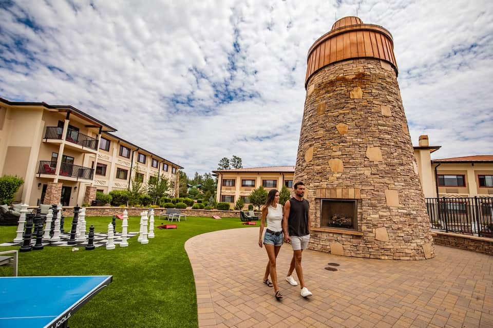 Couple walking past stone lighthouse tower with resort buildings and manicured lawn