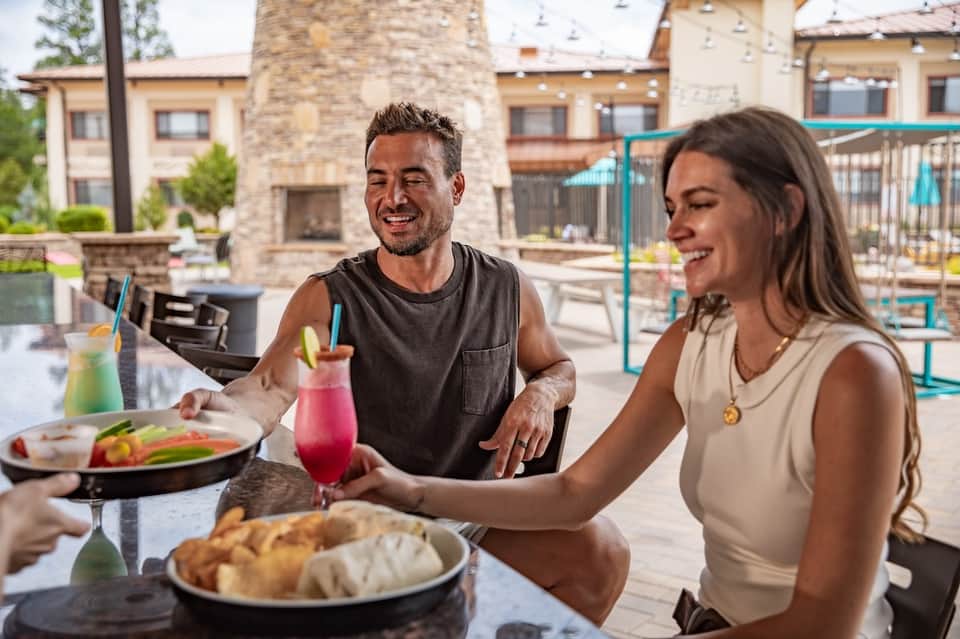Couple dining poolside at resort restaurant with colorful beverages and scenic pool background