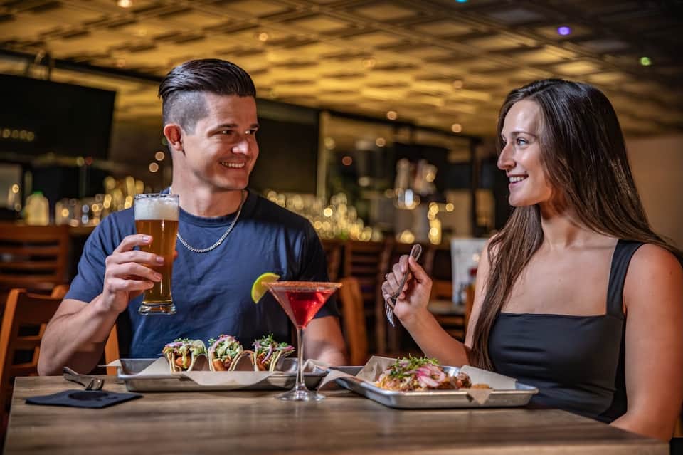 Couple dining together at restaurant bar with cocktails, appetizers, and warm ambient lighting