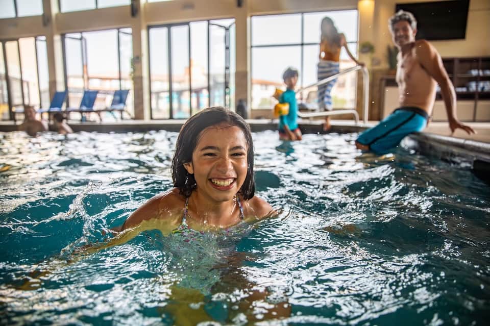 Family enjoying indoor heated pool with floor-to-ceiling windows and sea view in background