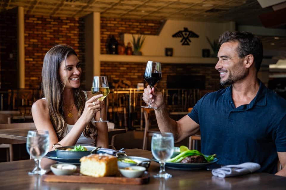 Couple toasting with wine glasses at restaurant table with plated meals