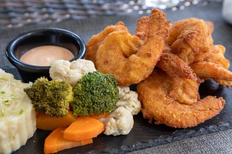 Fried shrimp with cauliflower, broccoli, carrots and dipping sauce on dark slate plate