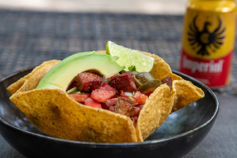 Ceviche served in crispy tortilla cup with avocado, lime, and local beer nearby