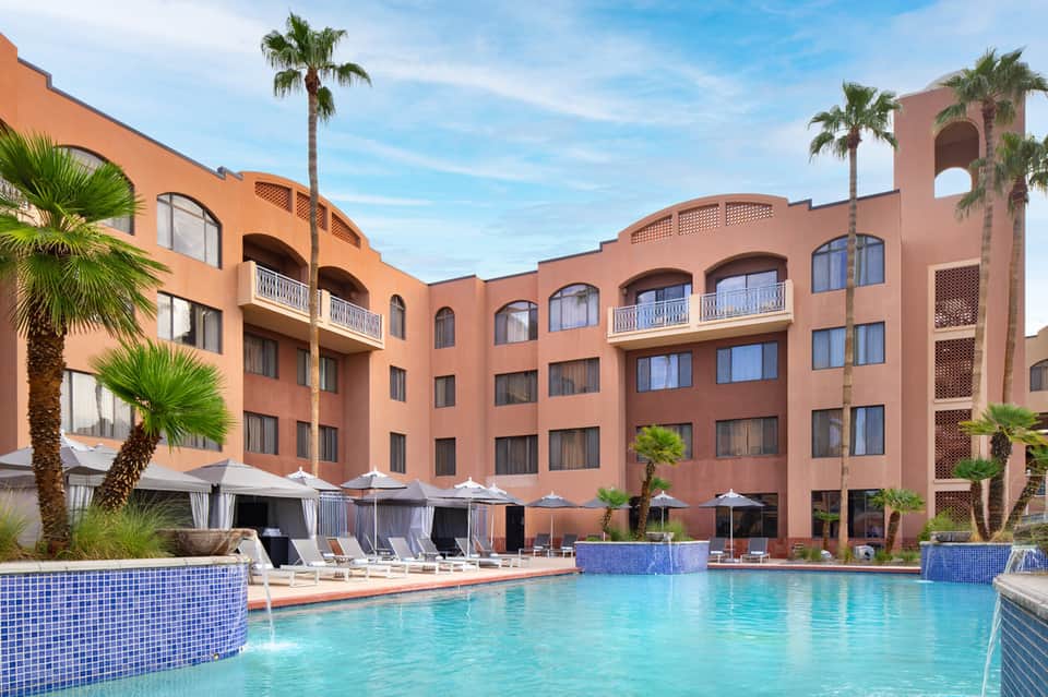 Tropical resort pool with terracotta architecture, palm trees, and lounge seating