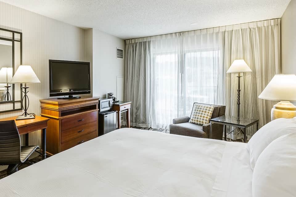 Hotel bedroom with white bedding, wooden furniture, TV, and balcony access