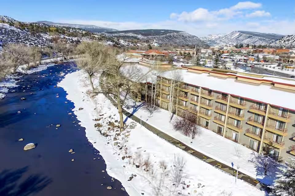 Riverside resort building on snowy banks with mountains, blue river, and winter landscape in background