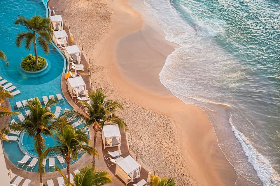 Beachfront resort aerial view with turquoise pools and palm trees along sandy shore