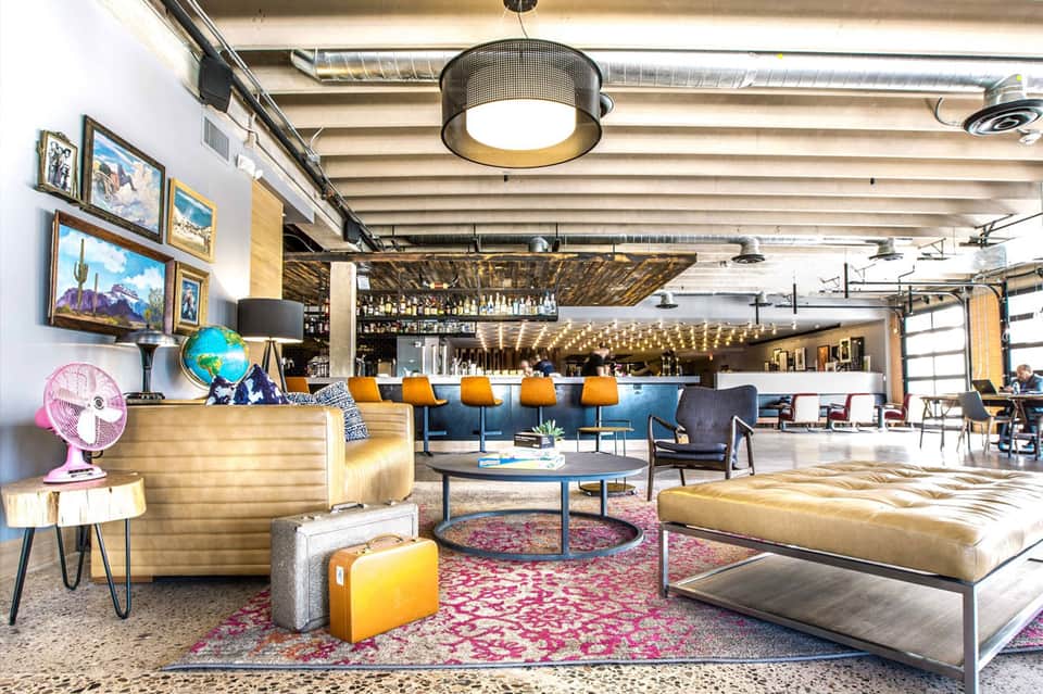 Contemporary hotel lobby with colorful furnishings, bar area, and eclectic artwork on white walls
