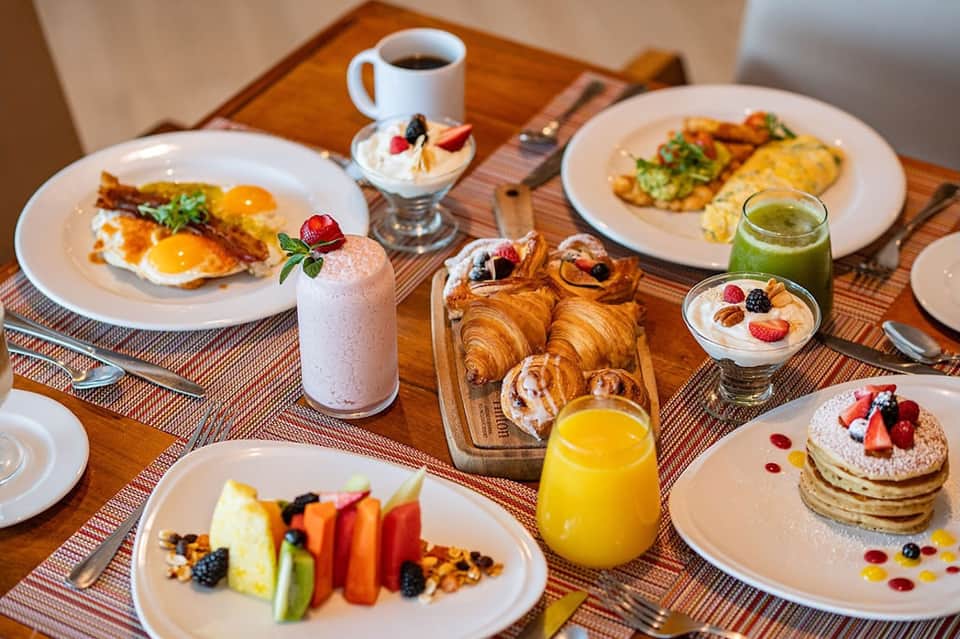 Hotel breakfast spread with eggs, croissants, pancakes, fresh fruit, juice, and coffee on wooden table
