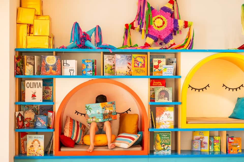 Colorful children's reading nook with orange alcove, shelves of books, and decorative hanging ornaments